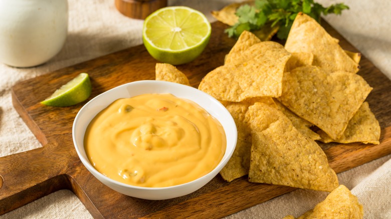 bowl of queso and tortilla chips on wooden cutting board