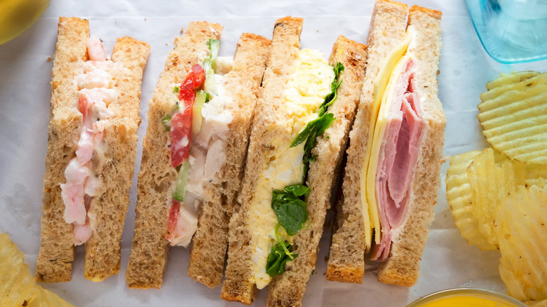 Four different types of sandwiches on a tray with potato chips.