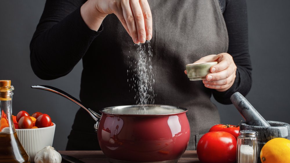 Chef seasoning a dish in a red pot