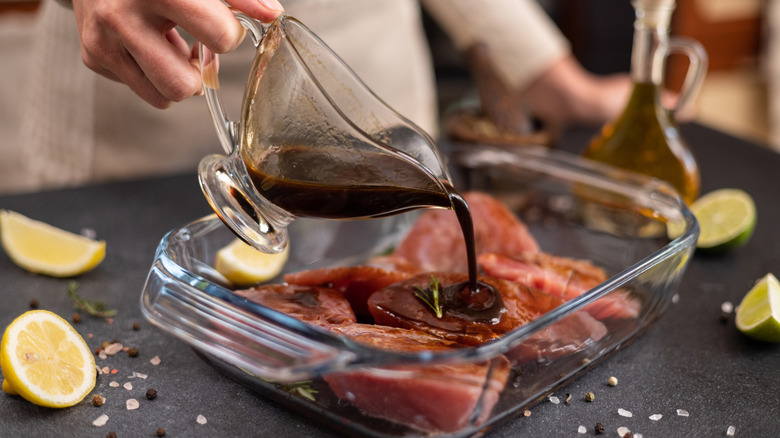 Hand pouring marinade into a glass dish with olive oil and lemon and lime slices on a plate nearby