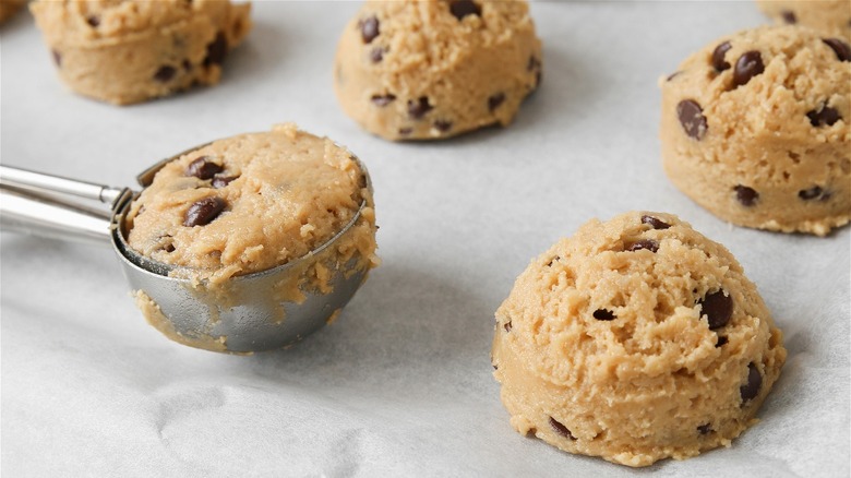 Cookie scoop with dough and balls of dough on baking sheet