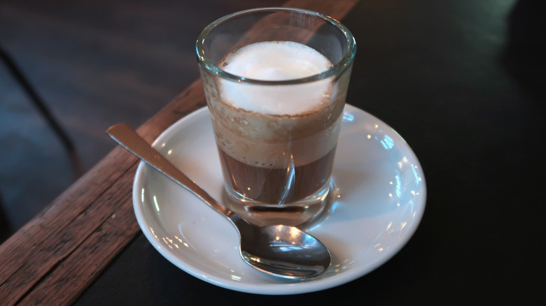 A short Macchiato sitting on a plate with a spoon