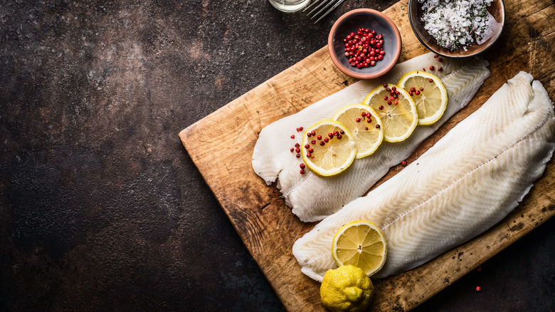 Raw white fish on wooden board with lemon and spices