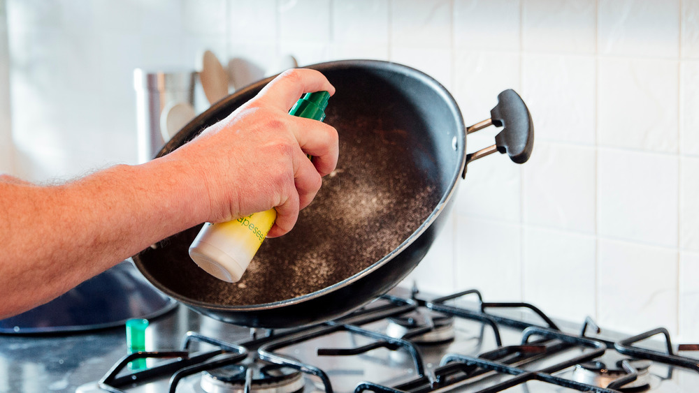 Man spraying pan with oil while cooking