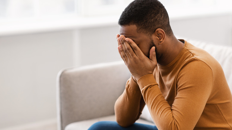 Depressed man sitting on couch covering his face