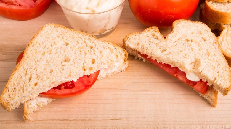 Tomato sandwich cut in half on wood surface surrounded by ingredients.