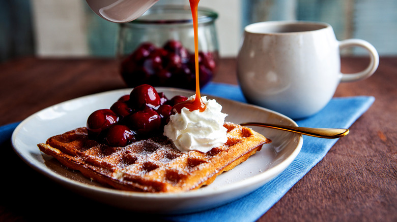 Drizzling caramel over a waffle with cherries