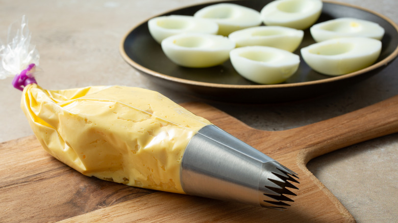 Deviled egg filling in piping bag next to empty hardboiled eggs