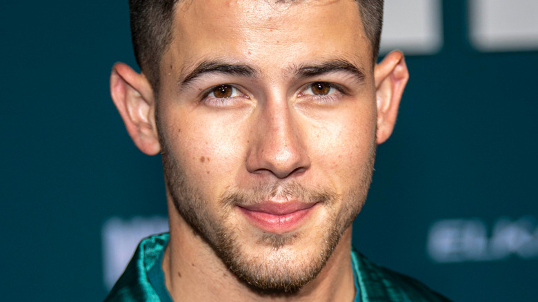 Nick Jonas wearing a green suit and posing at an event