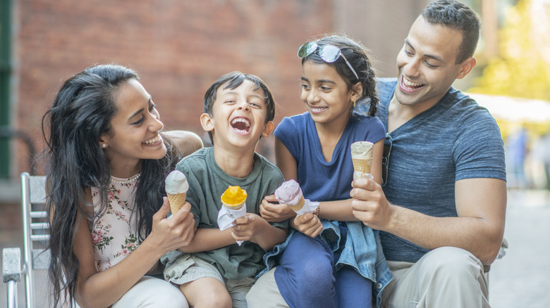 A woman, man, boy, and girl sitting together with ice cream cones in hand smiling and laughing.