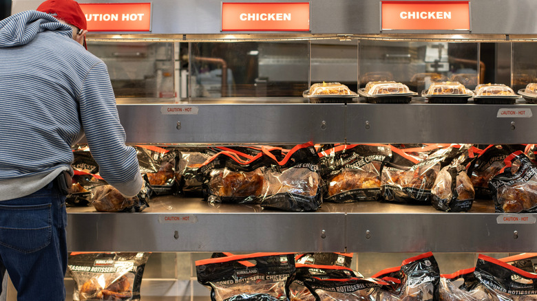 Man taking rotisserie chicken off shelf