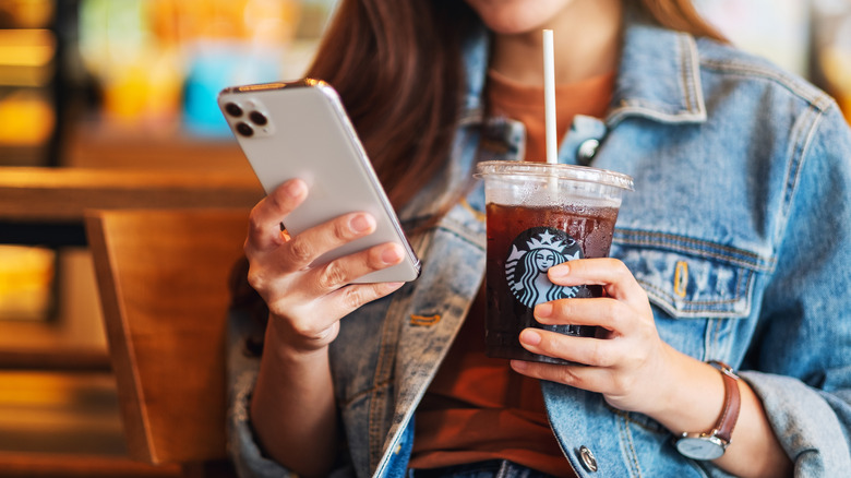 person looking at phone with starbucks drink