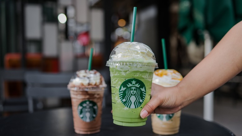 a hand holding one frappucino with two others on a table