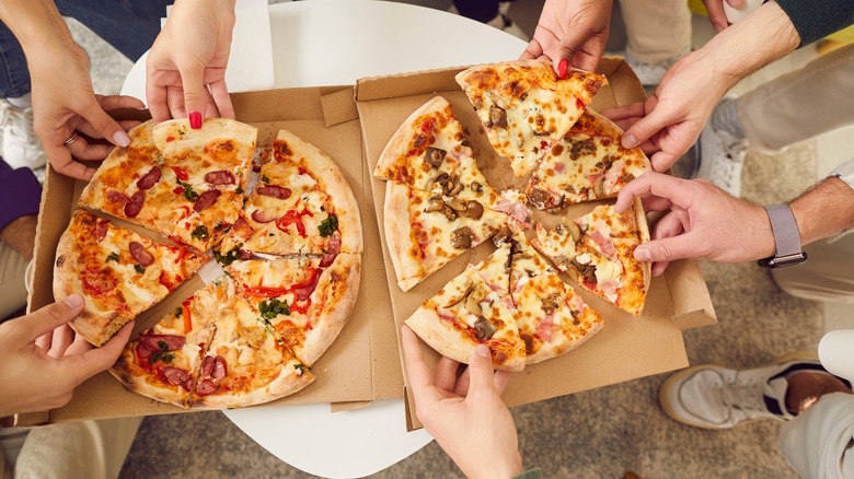People reaching for slices of pizza from open boxes
