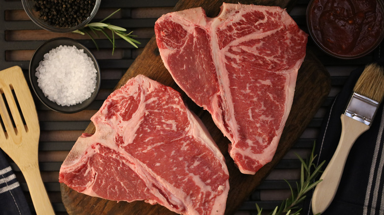 Two bright pink, raw porterhouse steaks on a cutting board.