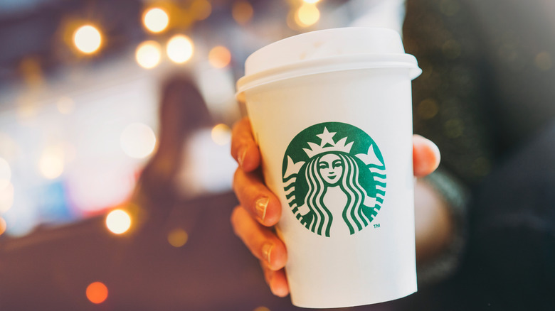 Person holding a white and green Starbucks cup