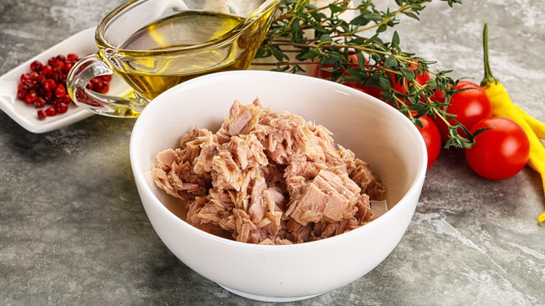 Canned tuna in white bowl with tomatoes, olive oil, and herbs next to it