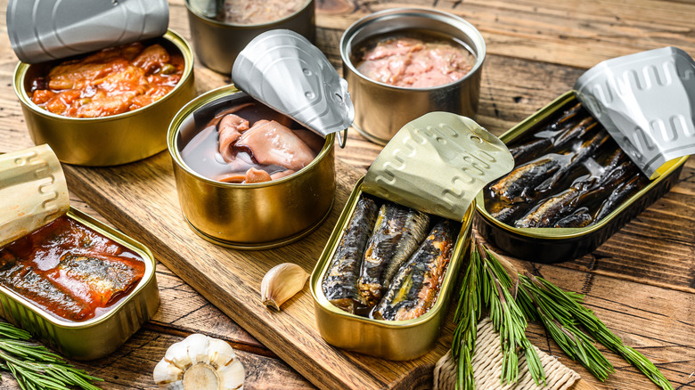 Canned fish products and herbs on wooden surfaces