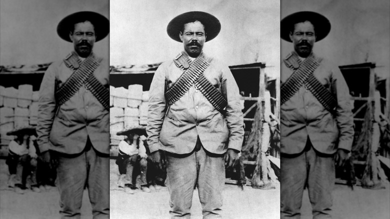 Pancho Villa looks directly at the camera in a black and white photograph with a bandolier of bullets crossed at this chest and a dark moustache.