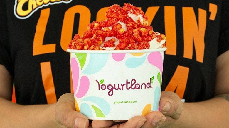 Person holding cup of yogurt with Cheetos
