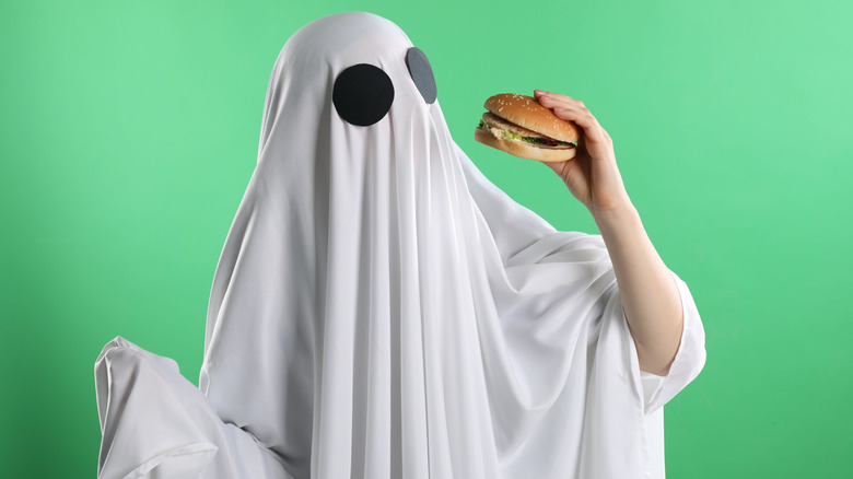 Person dressed as ghost eating burger.