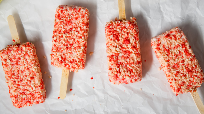 Four strawberry shortcake flavored popsicles on sticks.