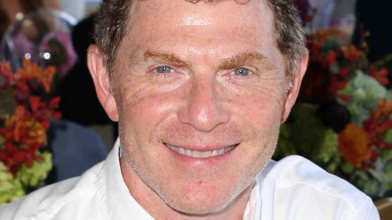 Bobby Flay wearing a white button down sitting and smiling