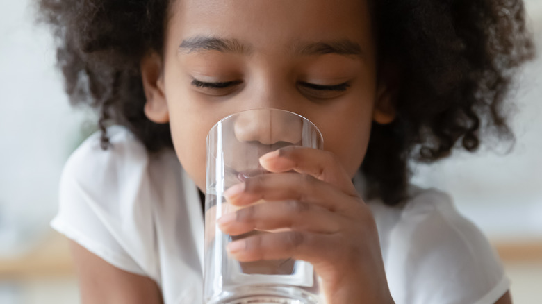 A young Black girl drinks a glass of water
