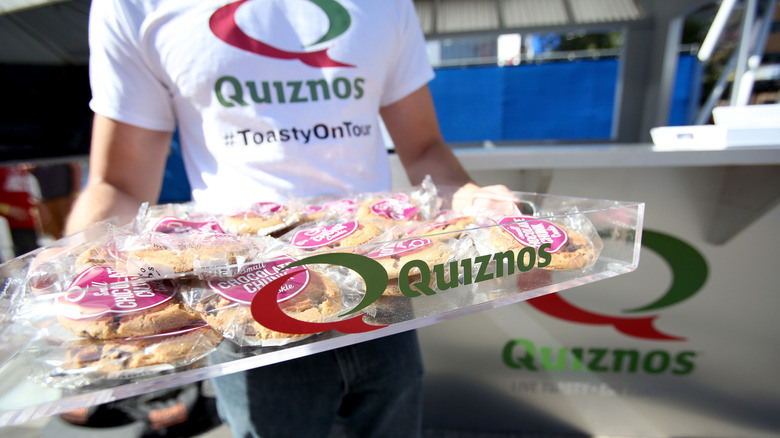 Man in Quiznos shirt carrying goodies from shop