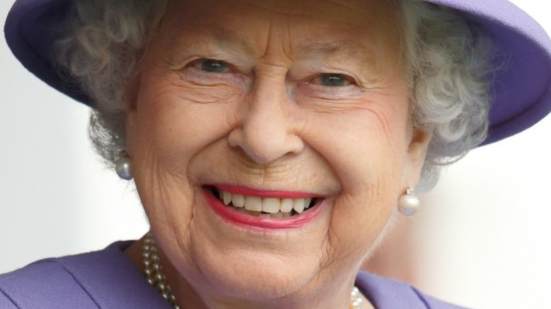 Queen Elizabeth smiling while wearing a purple hat and coat