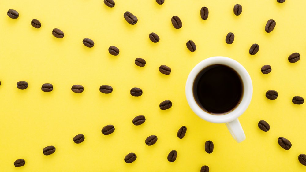 cup of coffee with coffee beans around it on a yellow background