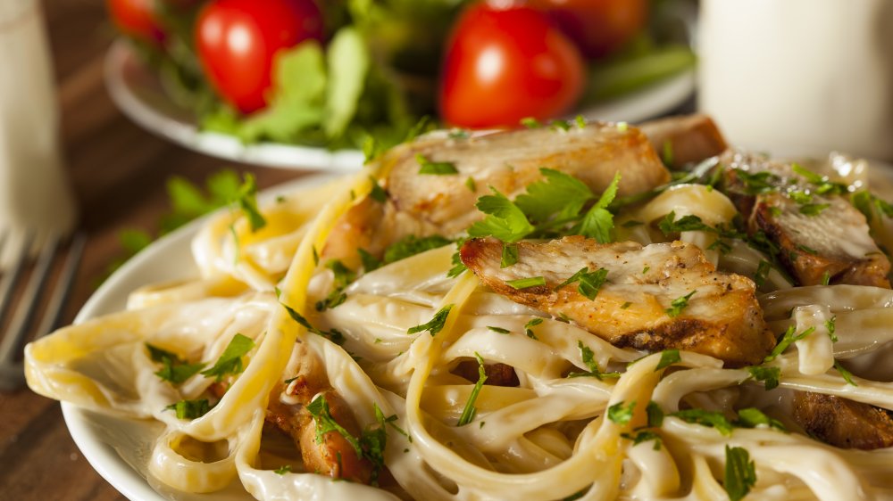Fettuccine Alfredo with chicken in a white dish with side salad