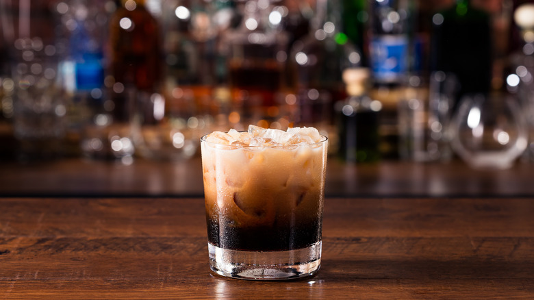 A glass with dark liqueur and cream on wood table