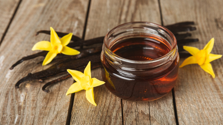 Vanilla extract in glass jar alongside vanilla pods and flowers