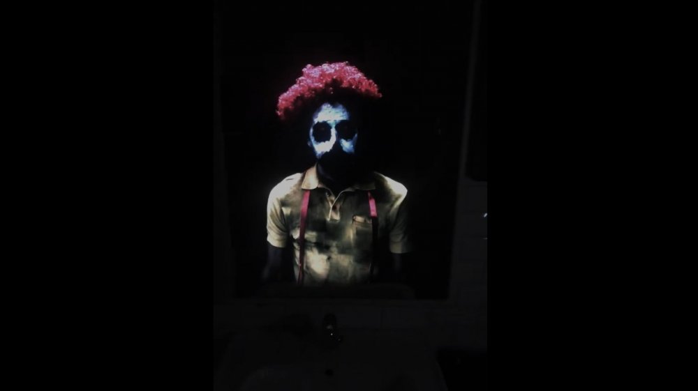 Creepy clown dressed similar to Ronald McDonald in mirror