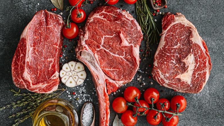 Raw steaks next to garlic and tomatoes