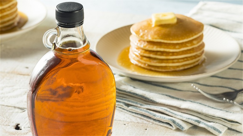 maple syrup bottle next to pancakes on plate
