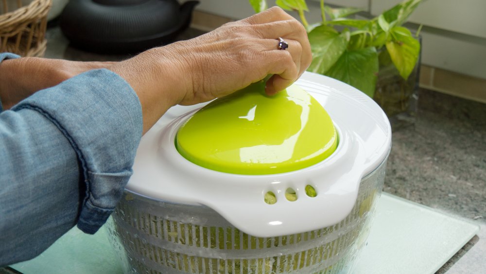 a woman using a salad spinner on the kitchen countertop