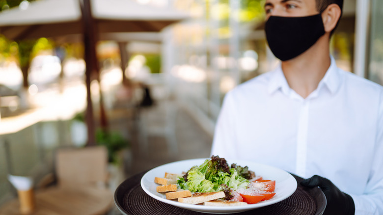 Waiter wearing a mask serving a salad