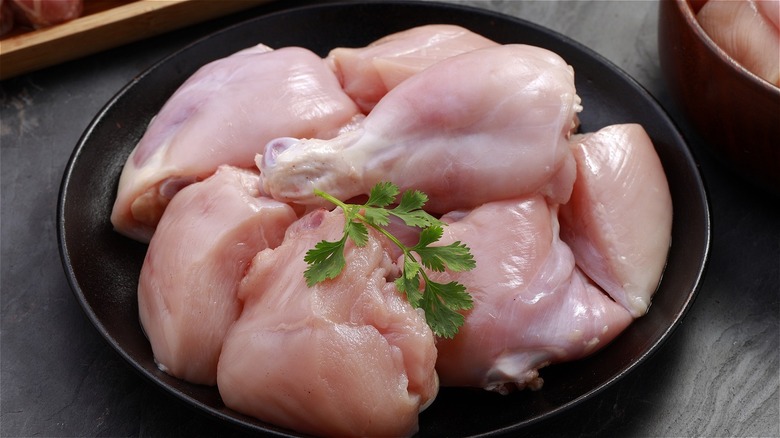 Raw chicken on a black plate with a sprig of parsley