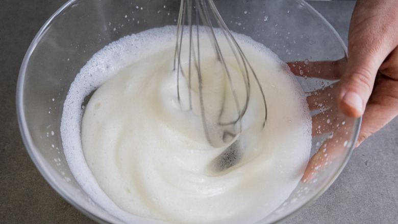 Hand holding glass bowl with egg whites being whipped