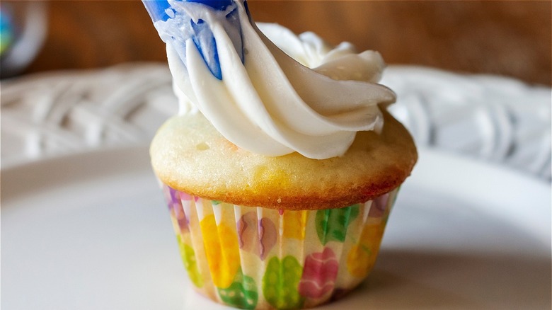 Icing being piped onto cupcake