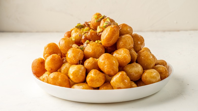 shallow white plate piled with round fritters topped with honey and chopped pistachios