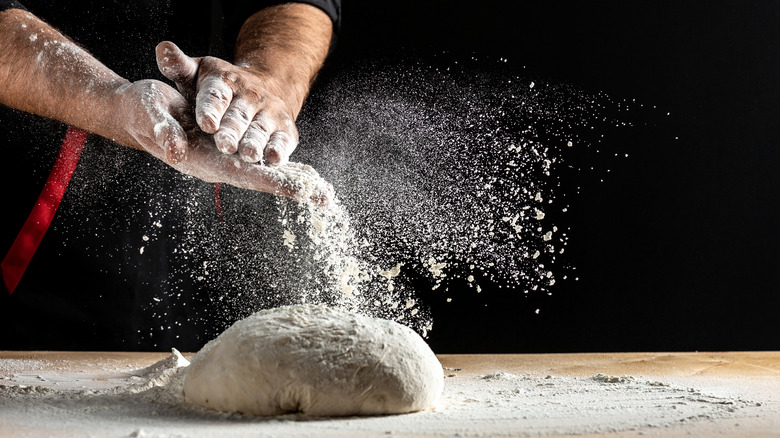 pizza dough on a wooden board with hands covered in flour