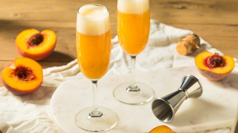 Peach Bellinis in flute glasses next to halved peaches
