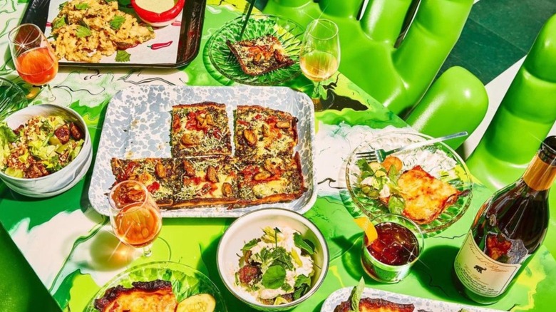 Spread of various food dishes and wine glasses on green table.