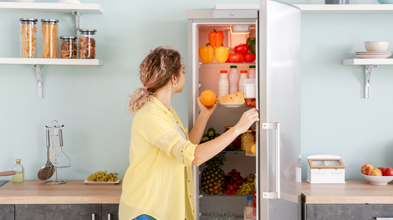 A woman taking an orange out of the fridge