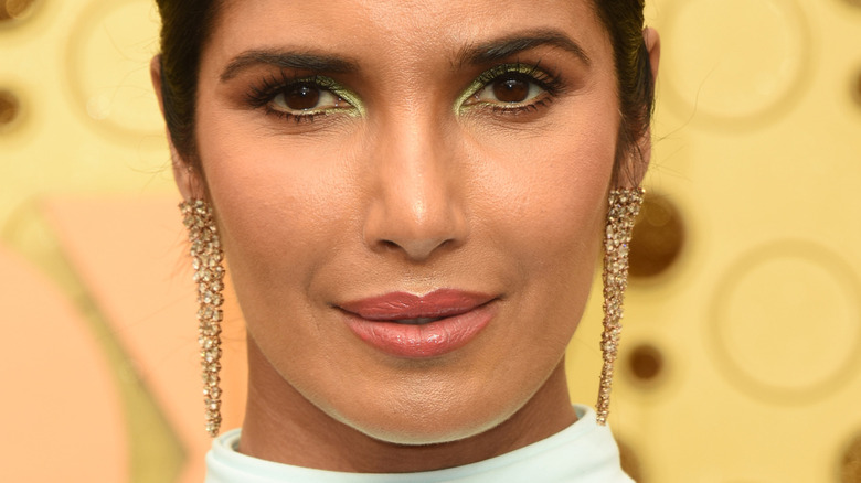 Padma Lakshmi smiling on the red carpet with green eyeshadow and dangly earrings