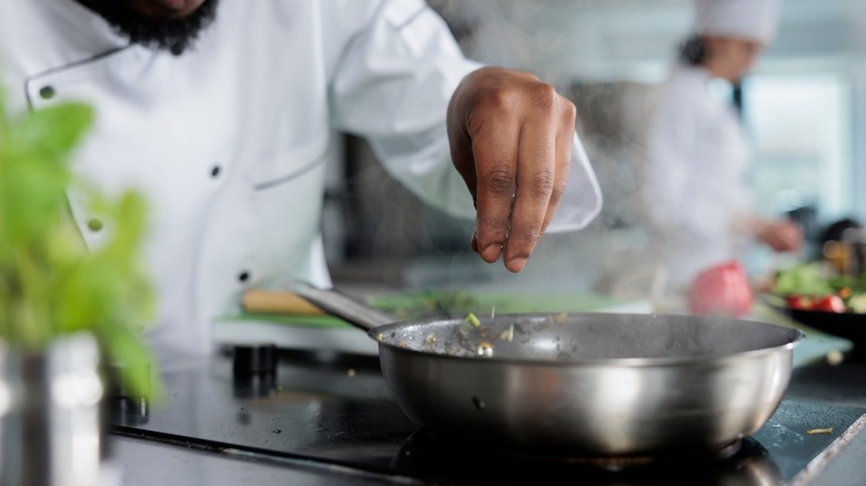 Chef sprinkling herbs into pan