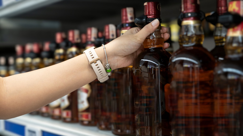 woman choosing a bottle of liquor from a store shelf